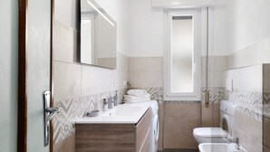 A modern bathroom with a sink, mirror, toilet, and washing machine.