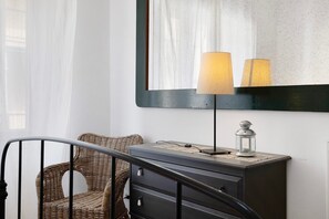 A room with a wicker chair, a dresser with a lamp, and a mirror on the wall.