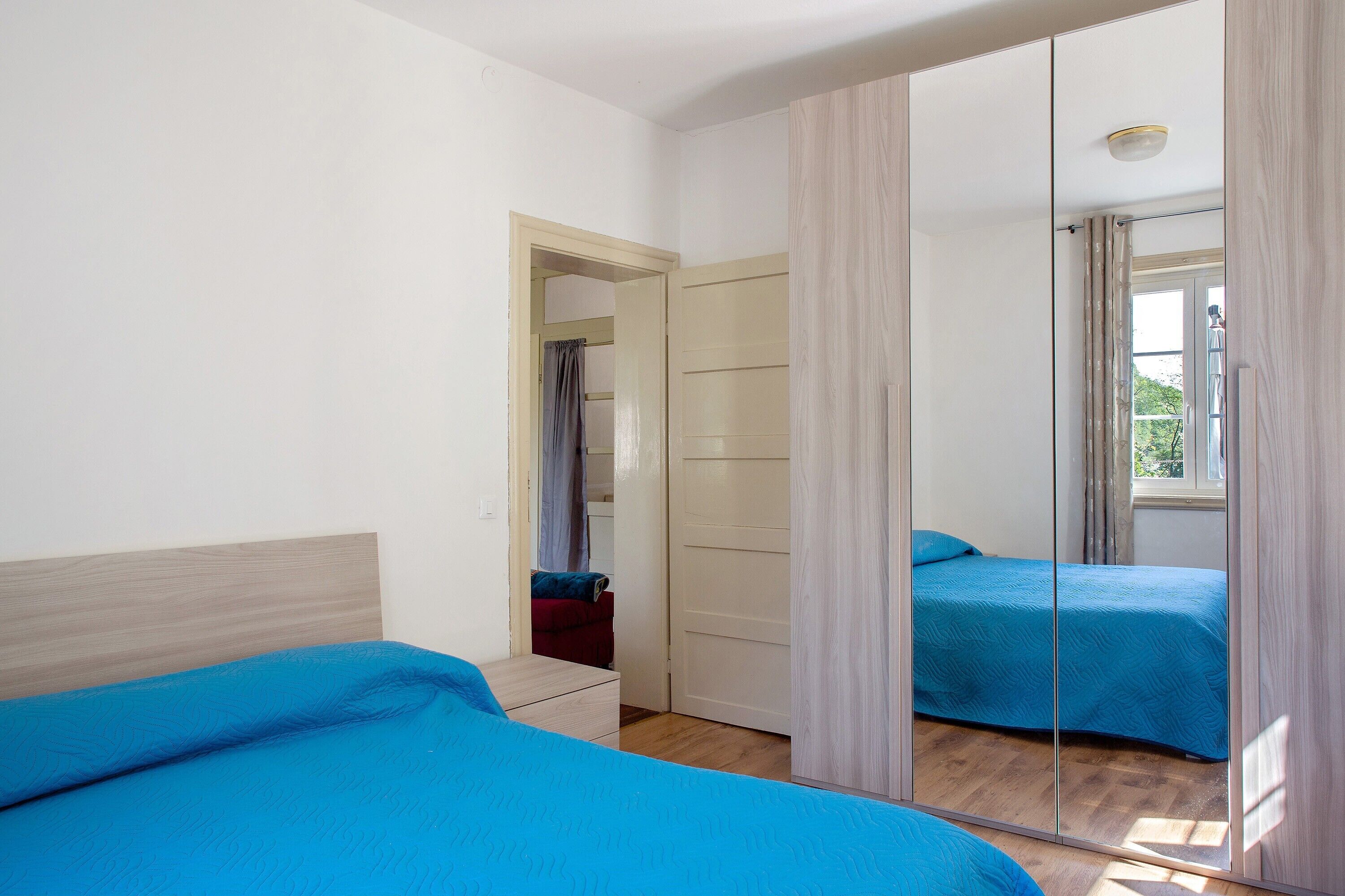 A bedroom with a mirrored closet, a bed with blue bedding, and a wooden floor.