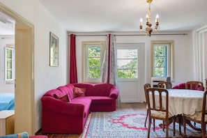 A room with a red sofa, a dining table with chairs, and two windows with curtains.