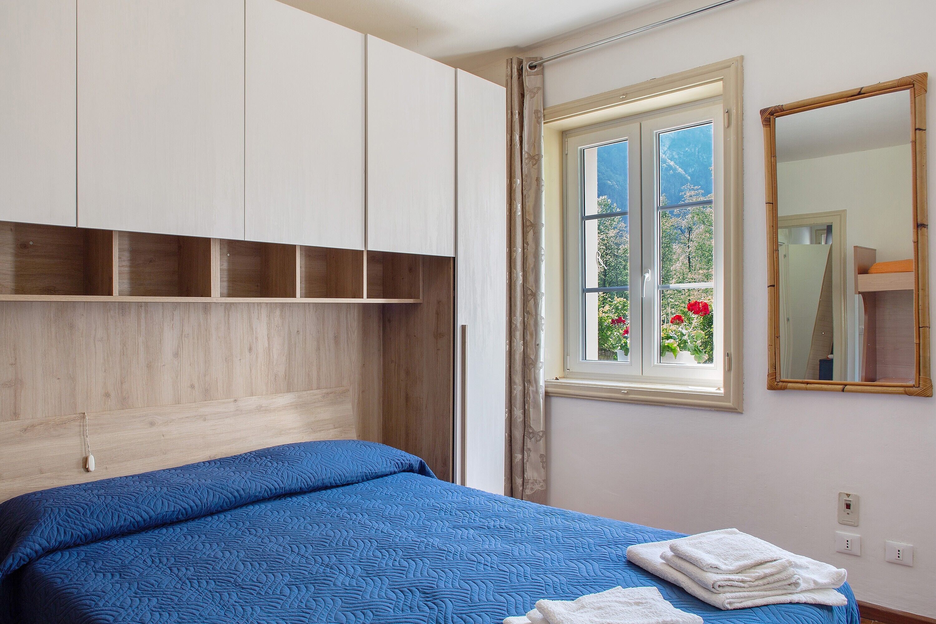 Ein Schlafzimmer mit einem Bett, einem Fenster mit Blick, einem Spiegel und eingebauten Holzausbau.