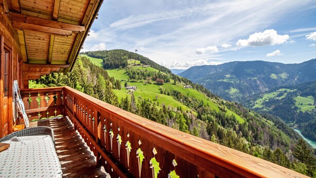 Ein Holzbalkon mit Blick auf ein grünes Tal und Berge.