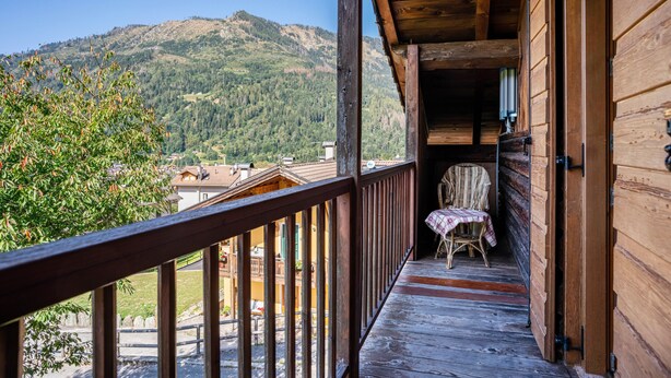 Un balcone in legno con vista su una montagna, una sedia e un tavolo.