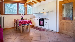 Una cucina con travi in legno, mobili bianchi, un tavolo da pranzo con sedie e vista dalla finestra.