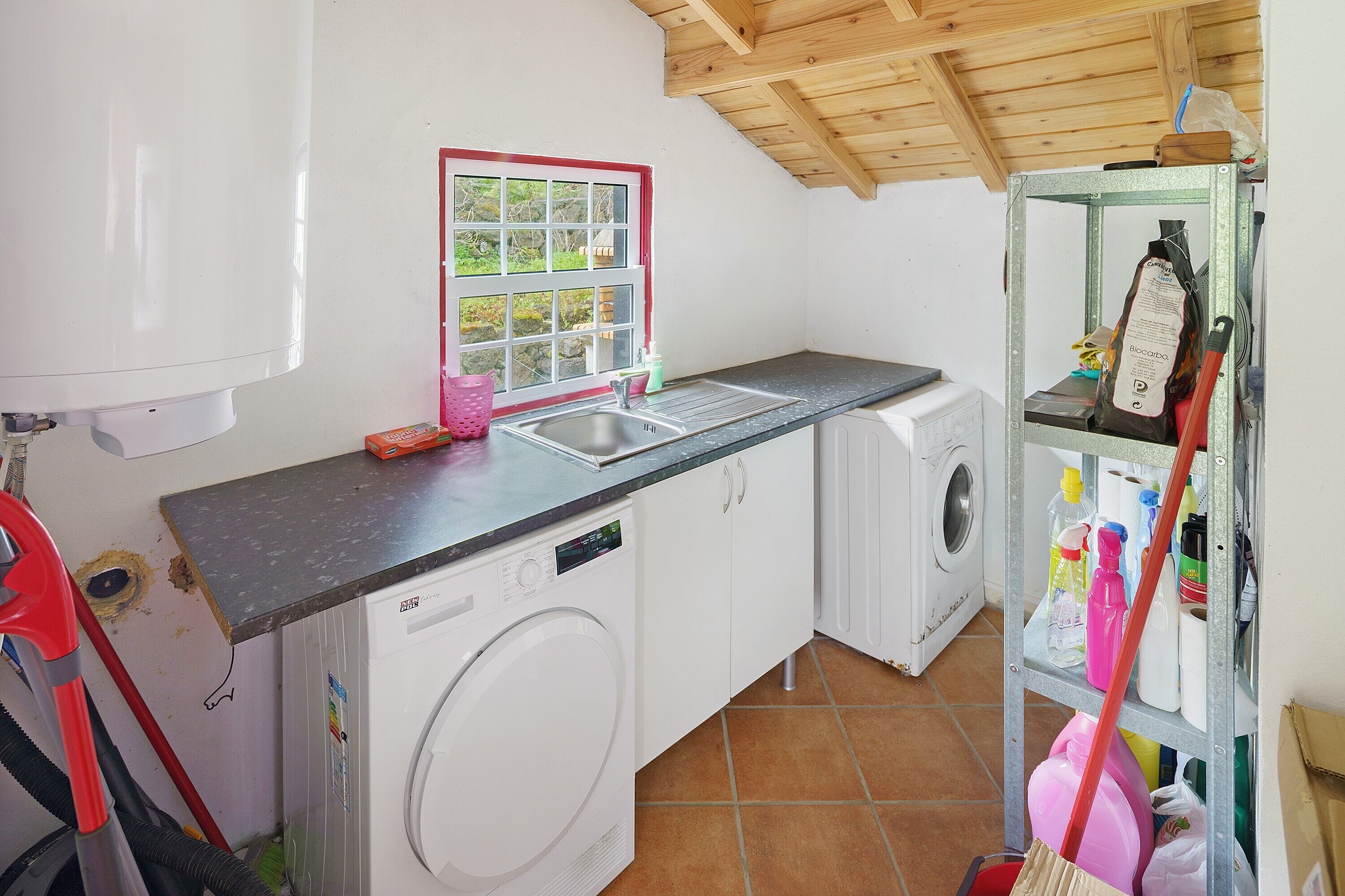 Cocina compacta con lavadora, un lavabo y una ventana con vistas a zonas verdes.