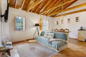 A room with a wooden ceiling, a bed, a desk with a lamp, a fan, and a window.