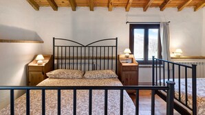 Een slaapkamer met een houten plafond, een bed met metalen frame, twee nachtkastjes met lampen en een raam met gordijnen.