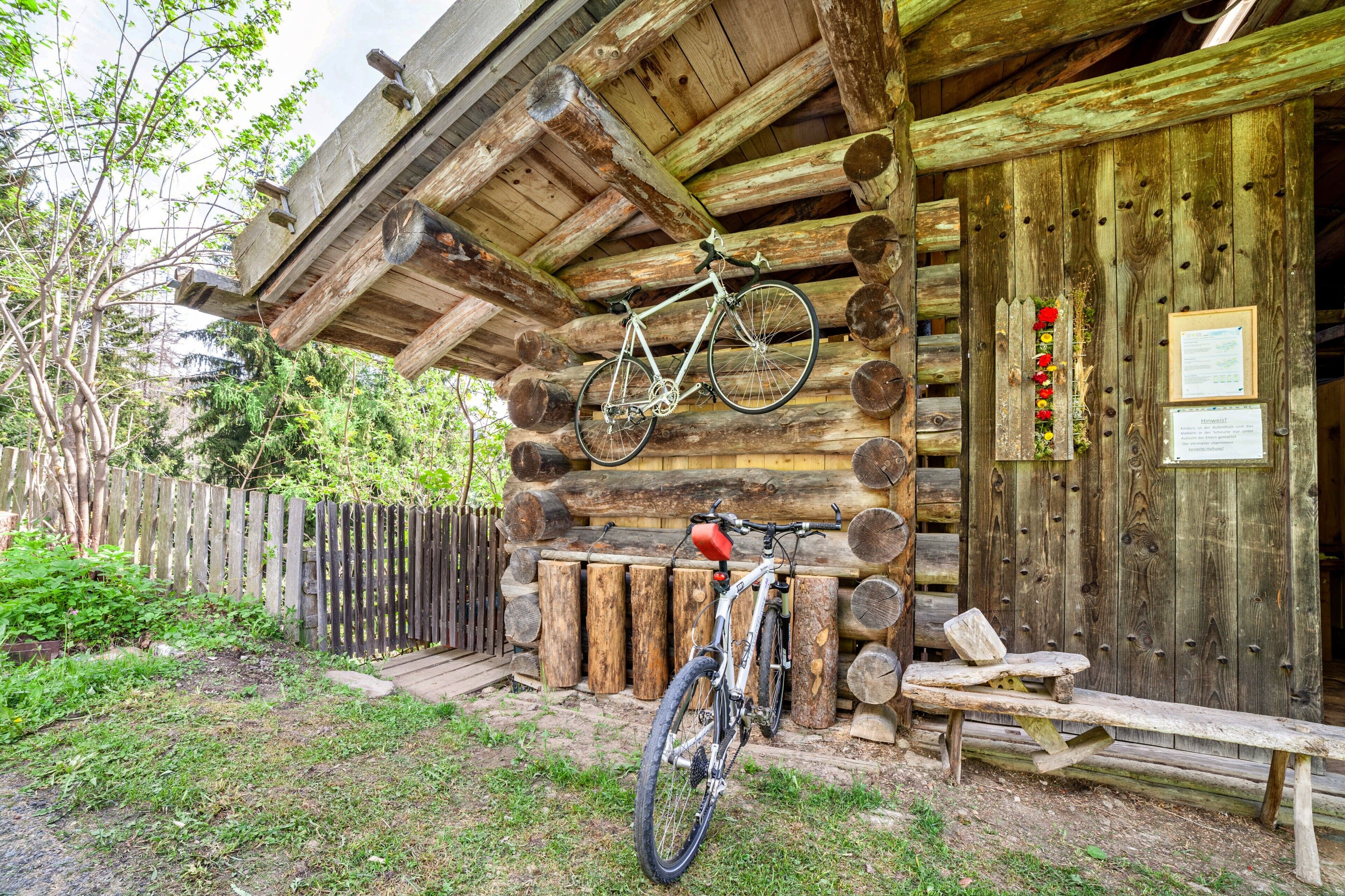 Una cabaña de madera rústica con una bicicleta colgada en la pared y un banco afuera.