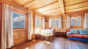 L’intérieur d’un chalet en bois comprend une table à manger, un canapé et de grandes fenêtres donnant sur les montagnes.