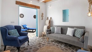 Een kamer met een blauwe fauteuil, een grijze bank, een houten plafond, een lamp en een blauwe deur.