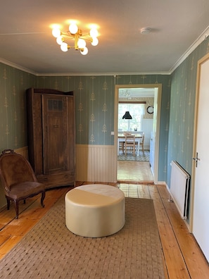 Una habitación con un armario de madera, una silla marrón, un reposapiés blanco y un suelo estampado.