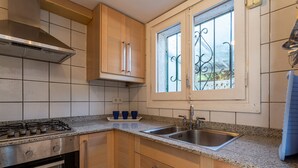 Una cocina con armarios de madera, un lavamanos de acero inoxidable y una ventana con rejas decorativas de hierro.
