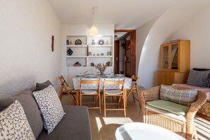 Een gezellige woonkamer met een bank, een eettafel met stoelen, een rieten fauteuil en een kast.