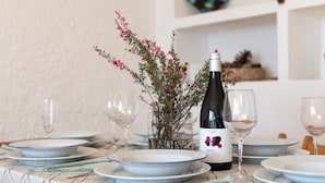 Una mesa de comedor puesta con platos, vasos, una botella de vino y un florero con flores.