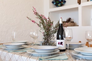 Une table à manger dressée avec des assiettes, des verres, une bouteille de vin et un vase rempli de fleurs.
