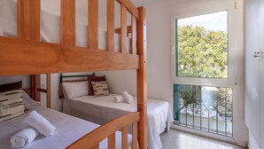 Una habitación con literas, un balcón con vistas a árboles y un ventanal grande.