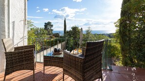 Una terraza con mobiliario de mimbre, una mesa de vidrio y vista al mar.
