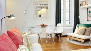 A modern living room with a sofa, chairs, a dining table, a bookshelf, and a lamp. - 4bnb - Serpenti Delightful Apartment (Rome)