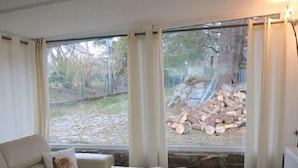 Una sala de estar acogedora con un sofá, una mesa de centro y vistas a un jardín a través de amplios ventanales.