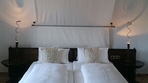 Una cama doble con sábanas blancas, dos mesitas de noche con lámparas y un dosel blanco en lo alto.