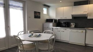 A compact kitchen with white cabinets, a microwave, a coffee maker, and a dining table with chairs. - Pacific Apartment (Fort-Mahon-Plage)