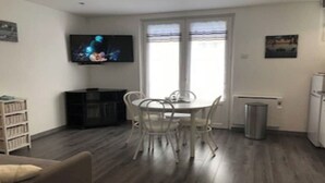 A compact living space with a dining area, a television mounted on the wall, and a refrigerator. - Pacific Apartment (Fort-Mahon-Plage)