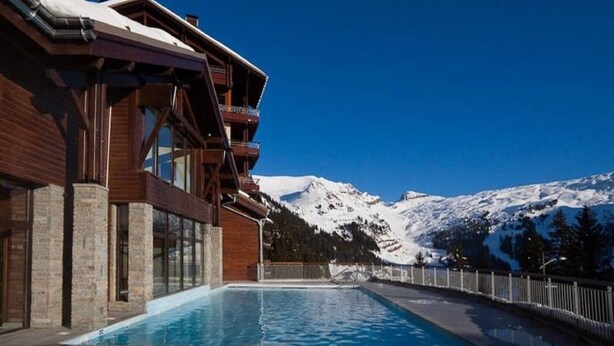 Un bâtiment moderne doté d’une piscine, de balcons en bois et offrant une vue sur des montagnes enneigées.