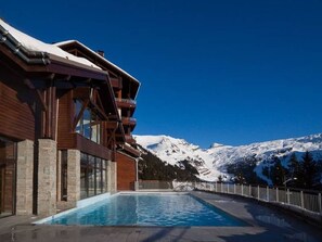 A modern building with a pool, wooden balconies, and a view of snow-covered mountains. - Terrasses d'Eos, Pierre & Vacances Premium, 5* Apartment for 4 people, 2 bedroom (Arâches-la-Frasse)