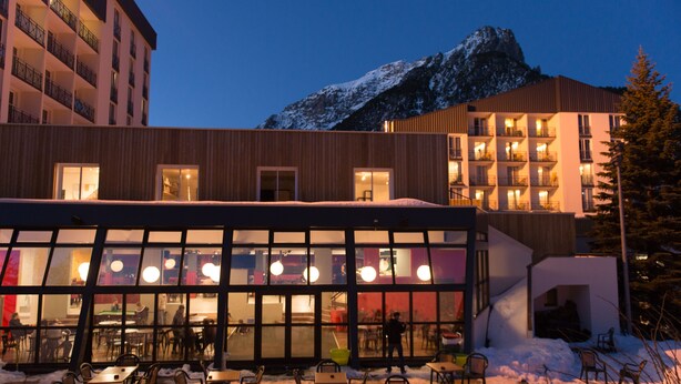 A modern building with large windows and a dining area with tables and chairs. - Village Club du Soleil de Montgenèvre (Montgenevre)