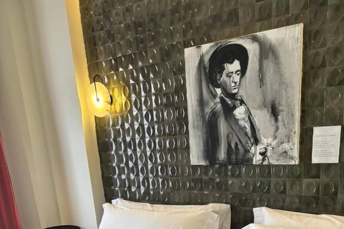 A hotel room with two beds, a wall-mounted artwork, a small table, and a lamp.