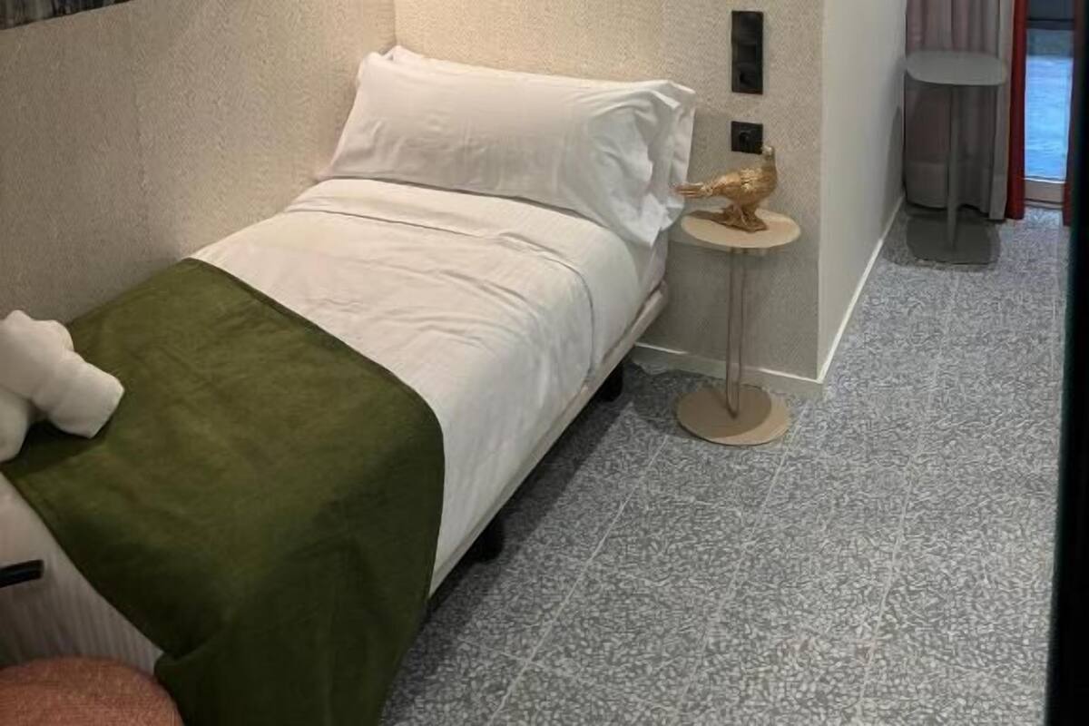 A hotel room with a bed, a wall-mounted artwork, a small table with a decorative item, and a view of a corridor with a door.