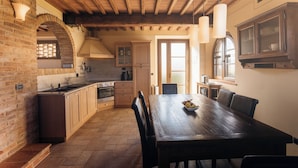 Een rustieke keuken met zichtbare houten balken, een bakstenen muur en een eethoek met een houten tafel en stoelen.