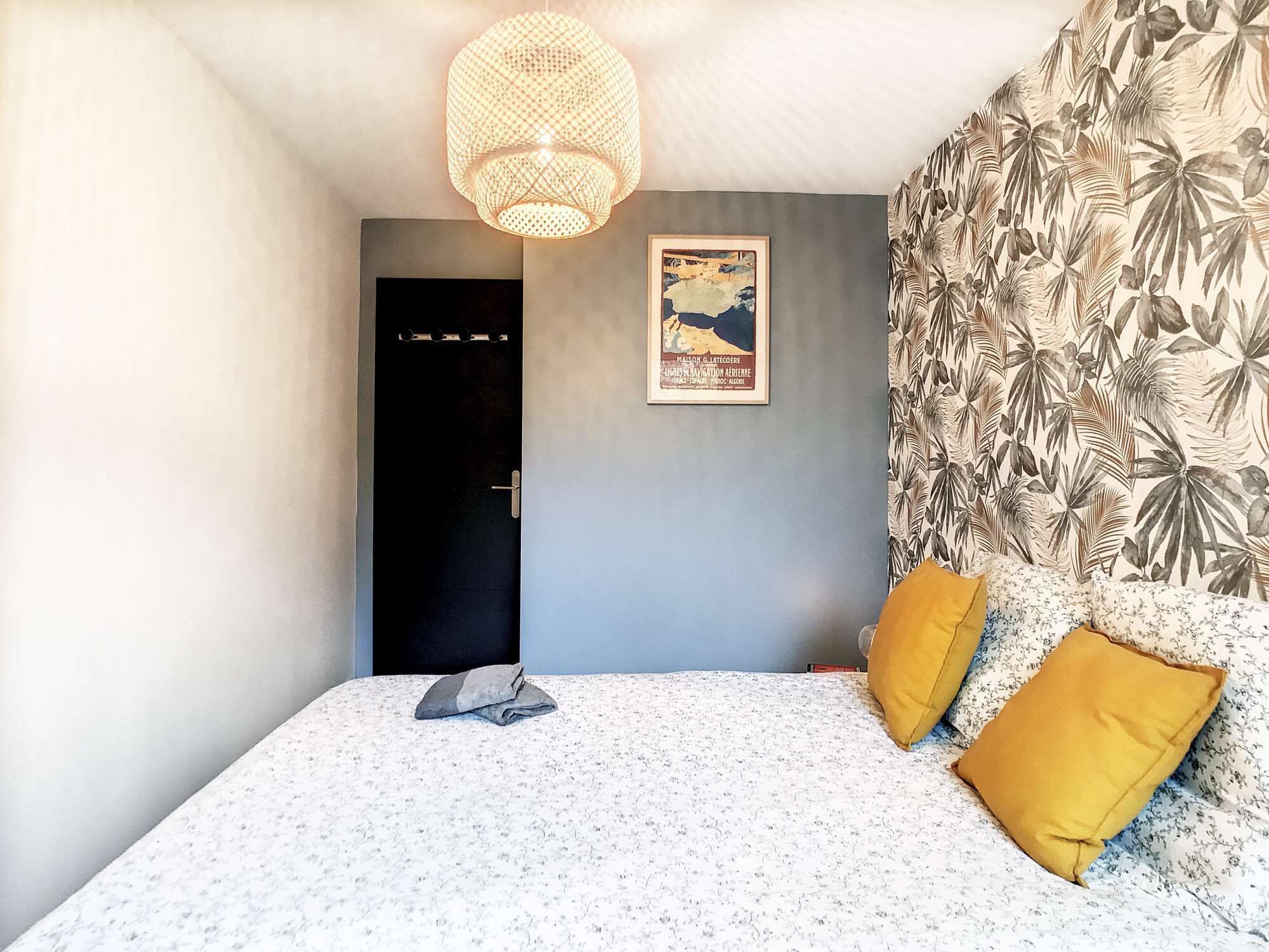 Een slaapkamer met een bed, een deur, een wandlamp en een muurdecoratie met tropische thema's.