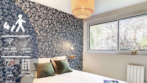 Quarto com cama, janela, radiador e parede com padrão de folhas.