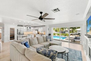 A modern living room with a sectional sofa, a ceiling fan, and a view of a pool. - Chestnut Court-3 BDR/2BA Water Direct Pool Home (Marco Island)