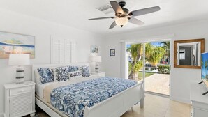 Un dormitorio con cama, mesita de noche, ventilador de techo y vistas al exterior.
