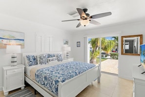 A bedroom with a bed, a nightstand, a ceiling fan, and a view of the outdoors.