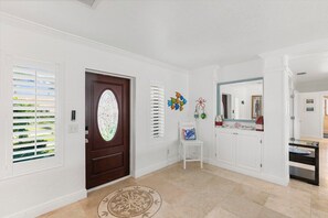 A hallway with a wooden door, white walls, a white chair, a small table, and a mirror.