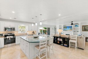 A spacious kitchen with white cabinetry, a central island with seating, and a dining area with a table and chairs. - Chestnut Court-3 BDR/2BA Water Direct Pool Home (Marco Island)