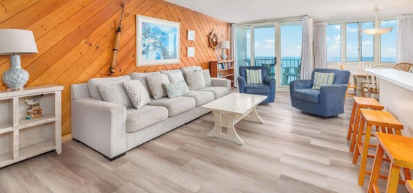 A living room with a sofa, armchairs, a coffee table, and a wooden wall with a framed picture.