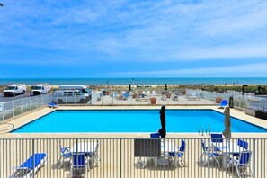 A pool area with a view of the beach, lounge chairs, and a lifeguard chair.