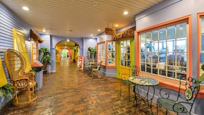 A corridor with brick flooring, wicker chairs, and tables, leading to a store with a large window.