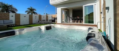 A swimming pool with a hot tub, a covered outdoor seating area, and a balcony with a view of the pool.