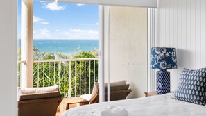 A balcony with a view of the ocean, a bed with white bedding, and a blue patterned lamp. - Seamist 6 - Apartment w/ocean views, 80m to beach (Sunrise Beach)