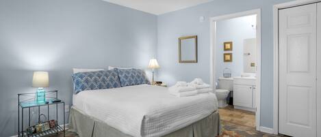 Un dormitorio con cama, mesitas de noche, lámpara, espejo y puerta que da a un baño.