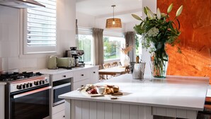A modern kitchen with a central island, a gas stove, and a dining area with a table and chairs. - Stockton House- light-filled retreat with art and unique flair (Daylesford)
