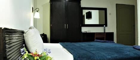 Un dormitorio con cama, mesita de noche, cómoda, espejo y puerta.