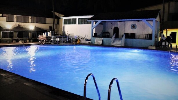 A swimming pool with clear blue water, surrounded by a building with a covered area and a staircase leading to an upper level.
