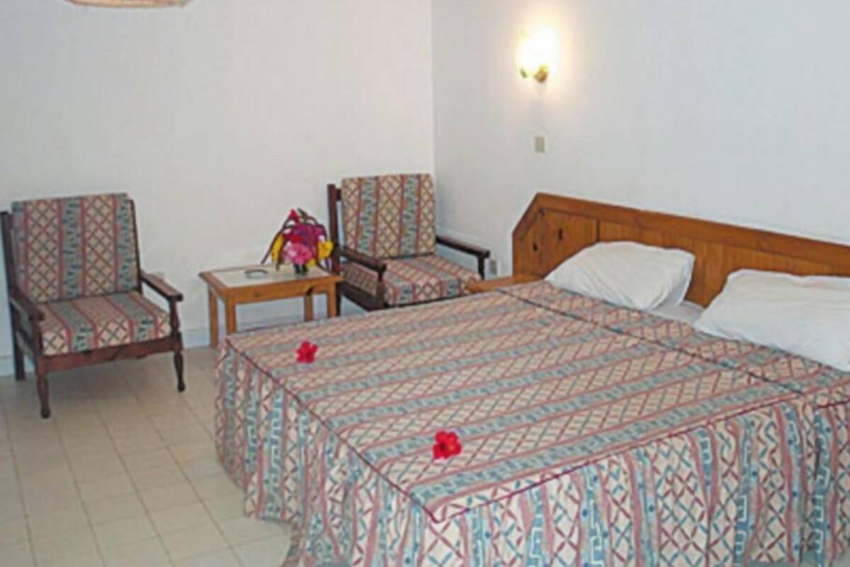 A bedroom with a bed, two chairs, a small table, a hanging lamp, and a wall-mounted light.
