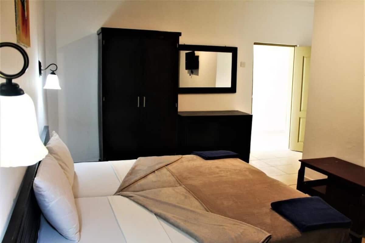 A bedroom with a bed, a wardrobe, a mirror, and a bedside table.
